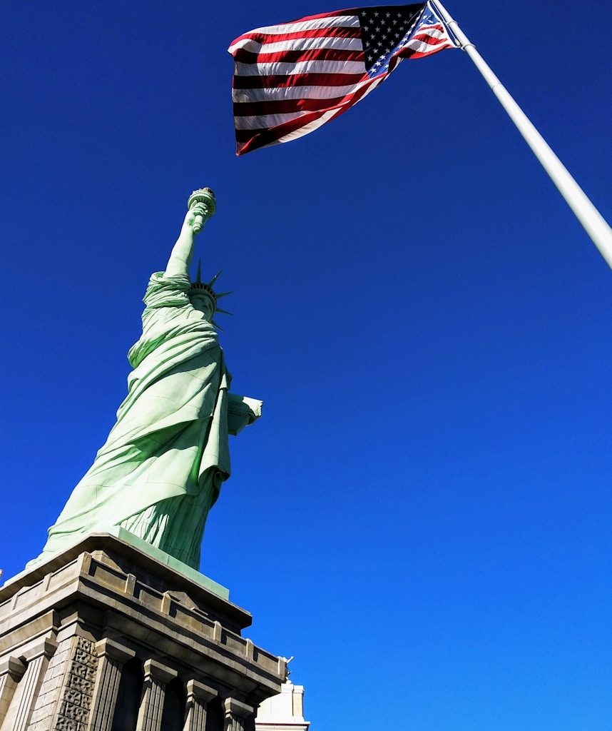 Statue of Liberty in front USA flag under blue sky