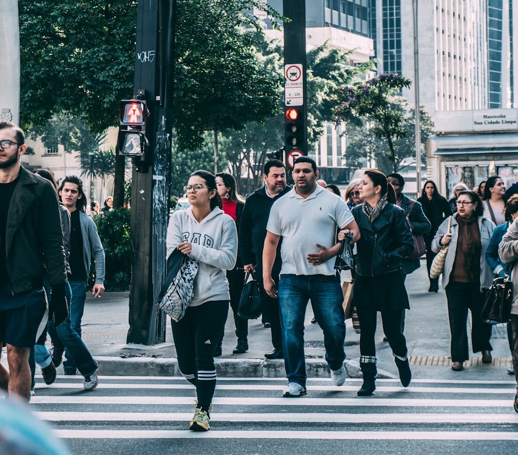 A diverse group of people crossing a street in a bustling city setting with skyscrapers.