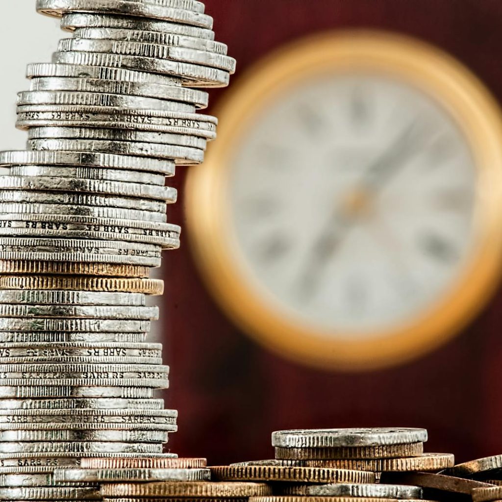 A close-up image of stacked coins with a blurred clock, symbolizing time and money relationship.