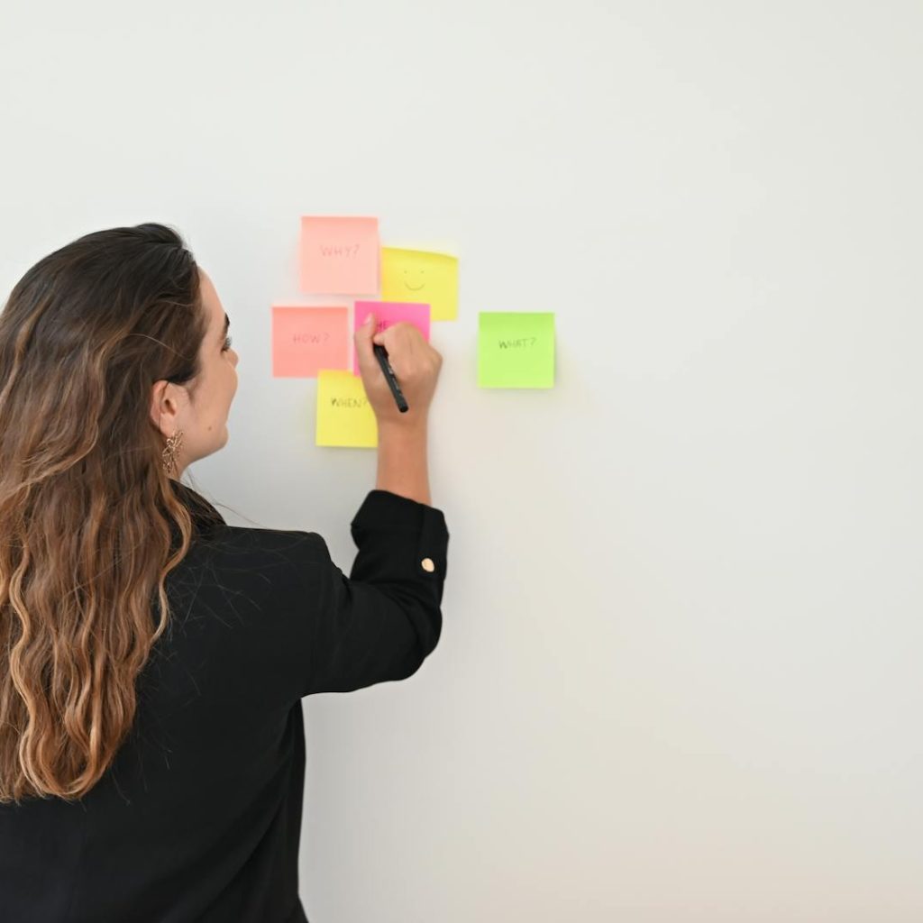 A businesswoman writes on colorful sticky notes on a white wall in an office setting.