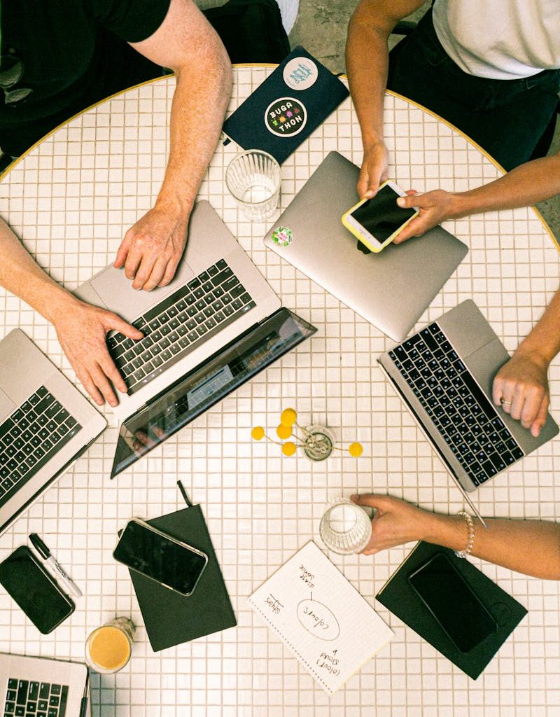 Top view of a team collaborating with laptops, phones, and notes in a modern office.