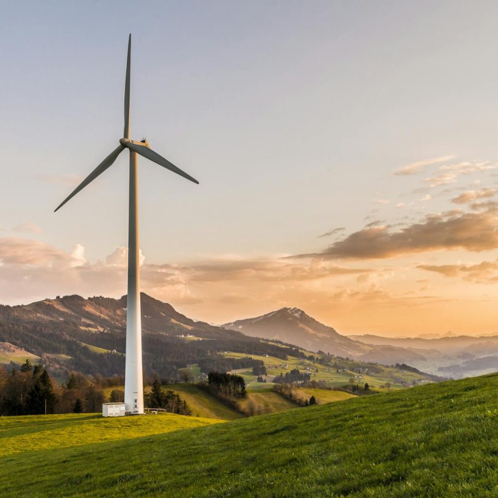 Wind turbine amid rolling hills and mountains at sunset, symbolizing renewable energy and sustainability.