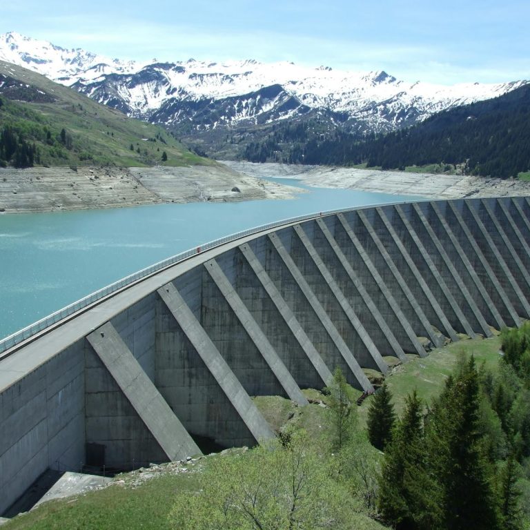 A breathtaking view of a dam amidst a serene alpine landscape with snow-capped mountains.