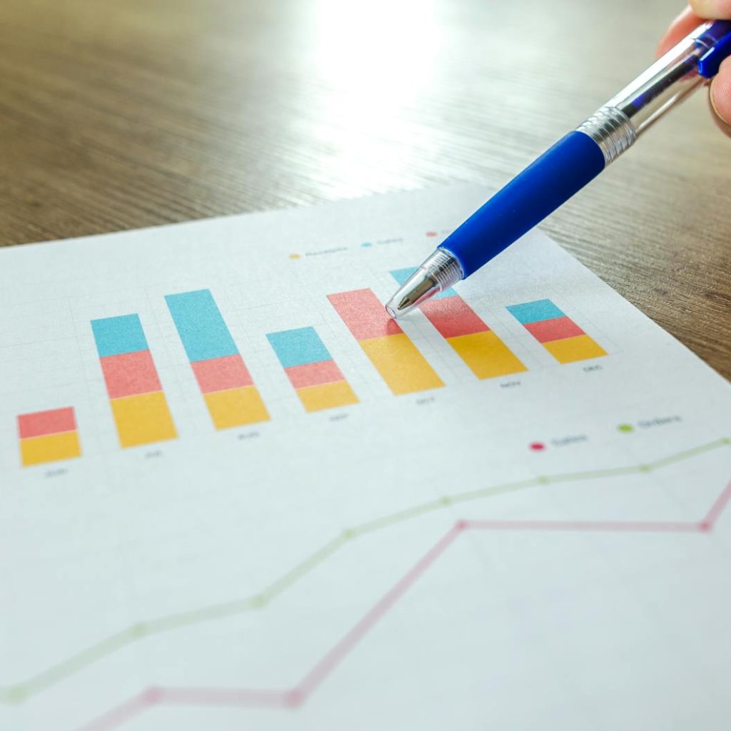 Detailed close-up of a hand pointing at colorful charts with a blue pen on wooden surface.